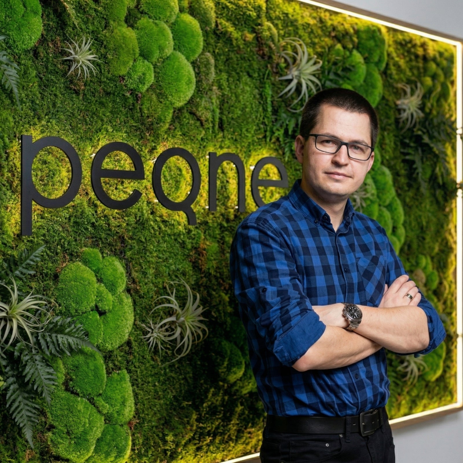 Michal Rajter v modrej károvanej košeli pri pozadí s logom peqne