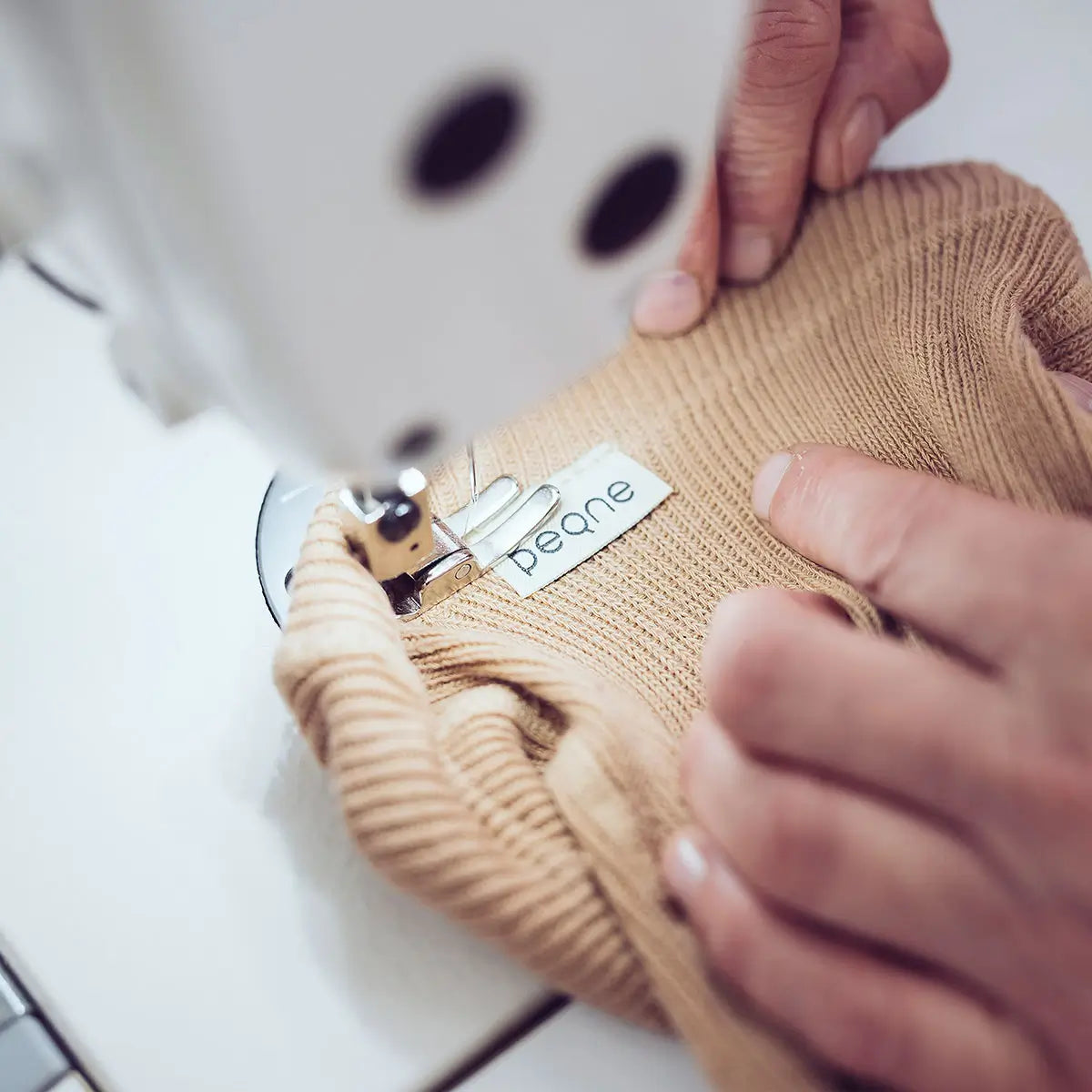 Detail šitia detských pančúch PEQNE, prišívanie značkového štítku na mäkký úplet počas ručnej výroby